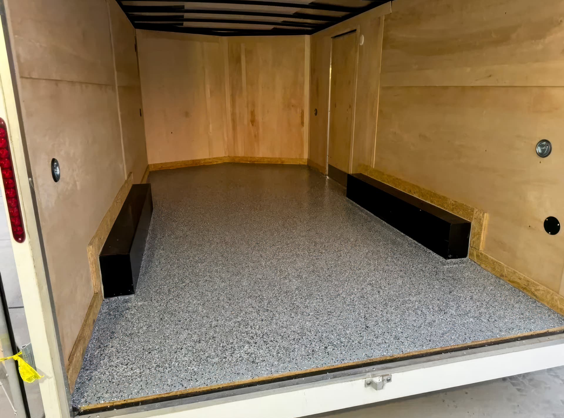 Light gray flake coating on the floor of a wood-lined enclosed trailer.